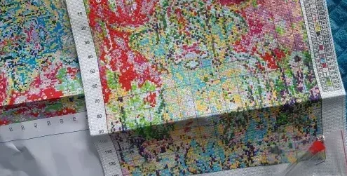 Buyer photo of the Highland Cow kit received: the color-printed fabric with its stitching grid and two chart sheets laid out on a quilted blanket